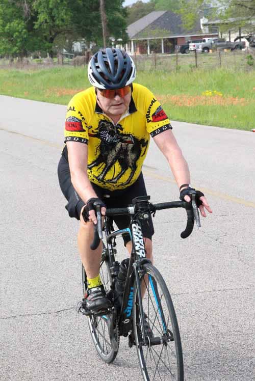 1. Male cyclist riding a road bike on a rural road wearing a yellow cycling jersey and helmet.
