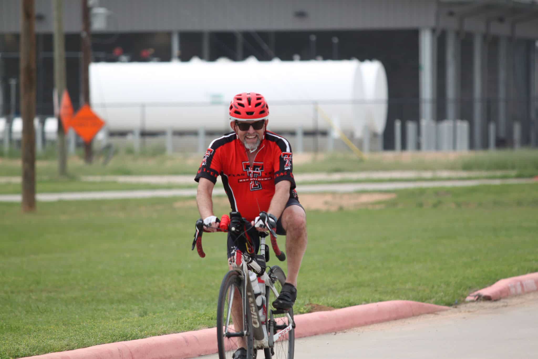 Bright red bike helmet and jersey, smiling cyclist enjoying outdoor riding on a road bike.