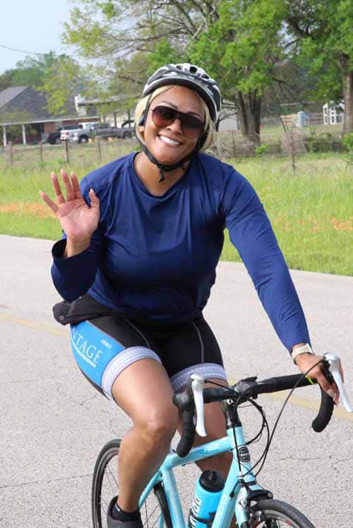Bike rider woman smiling in helmet and sunglasses on blue bicycle outdoors.