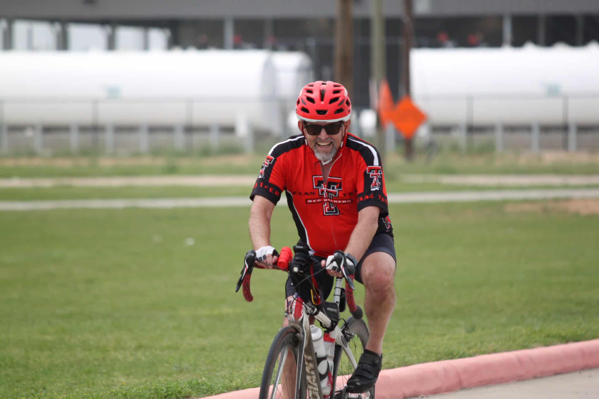 Vibrant cyclist wearing Texas Tech gear riding bike outdoors on a grassy track.
