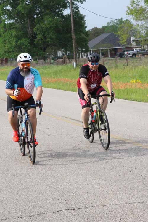 Brightly colored cyclists riding on a rural road during daytime, promoting Bluebonnet Express bike event.