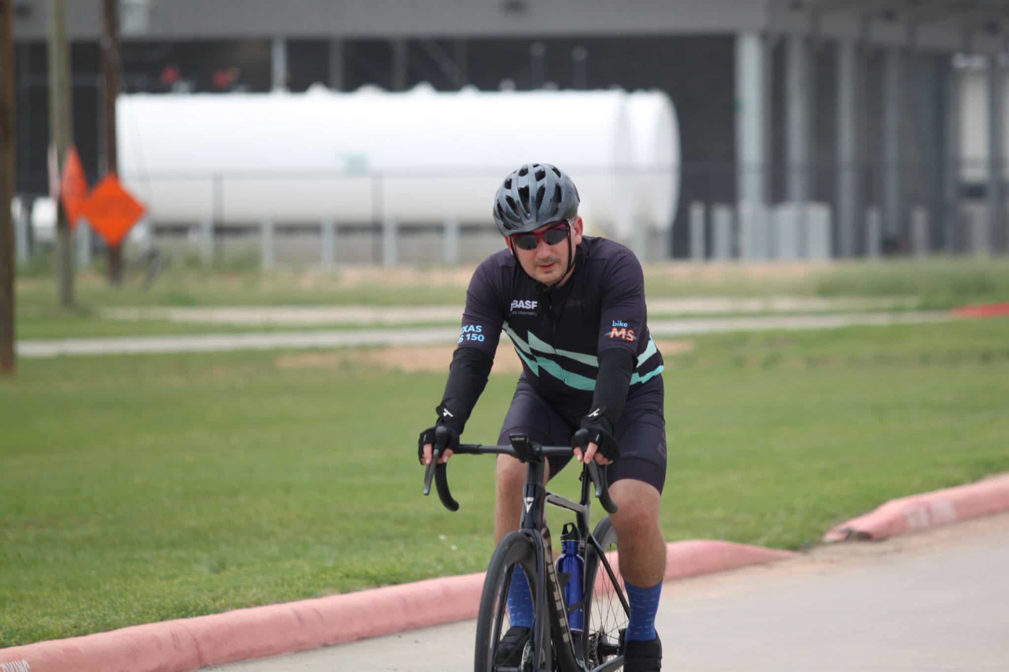 High-performance cyclist riding on the road with riding gear, helmet, and sunglasses.