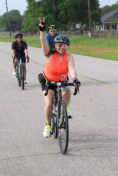 Bright female cyclist enjoying a fun ride on Bluebonnet Express bike trail, cheering with peace sign.