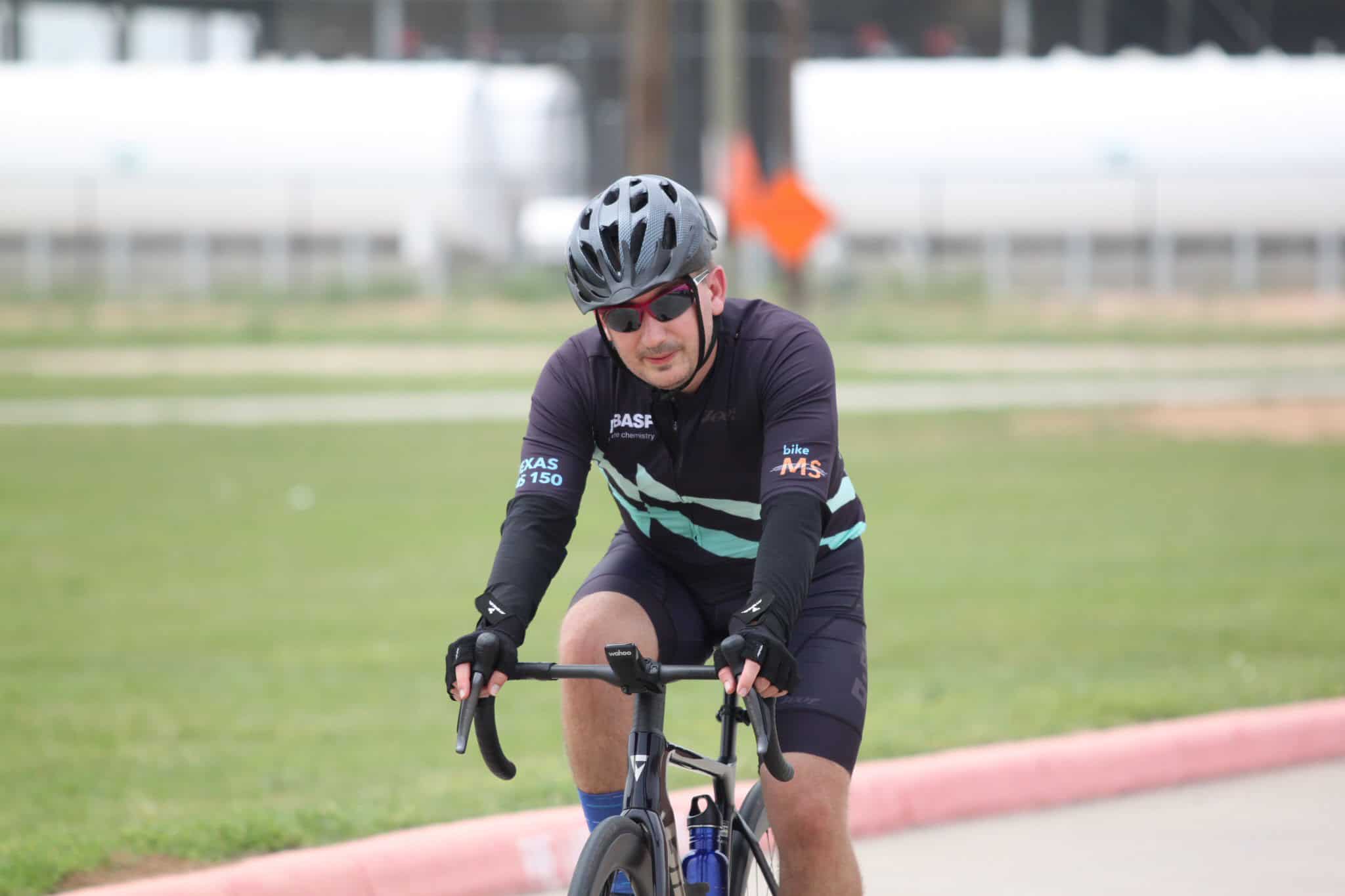 Bike rider wearing helmet and sunglasses on a blue and black bicycle, training for Bluebonnet Express cycling event.