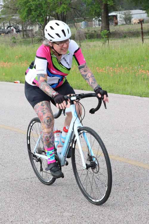 Bright female cyclist riding on scenic road, promoting outdoor biking and fitness.