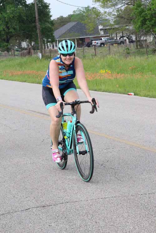 Bright female cyclist riding a blue bike on the road during daytime for Bluebonnet Express.