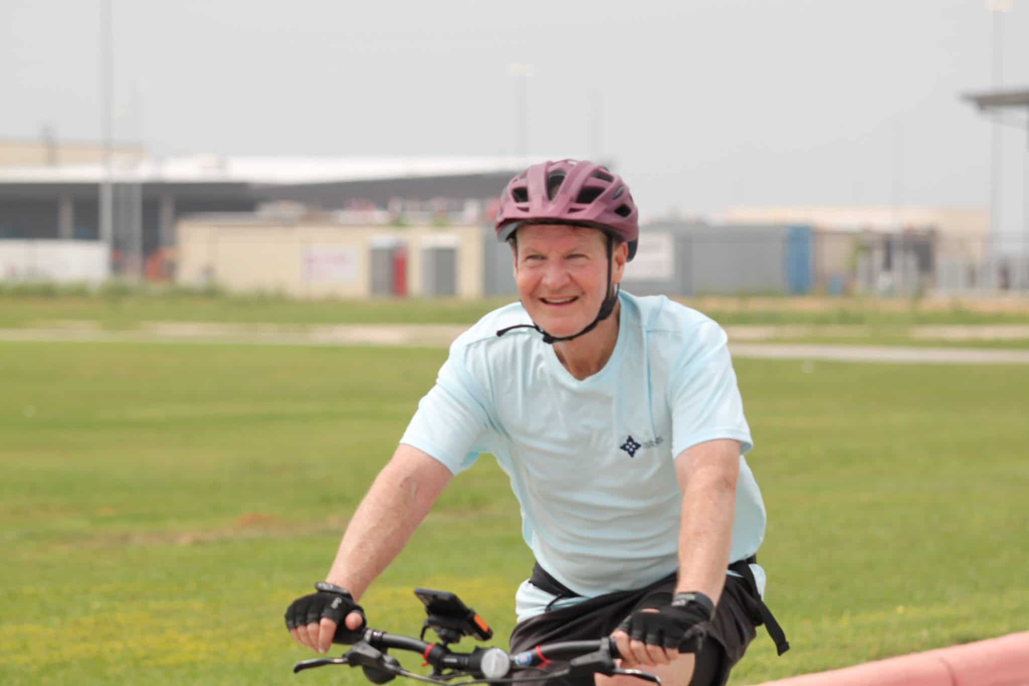 Man riding bicycle with pink helmet enjoying outdoor ride on grassy field.