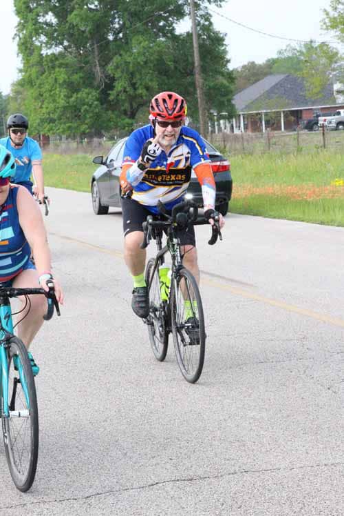 Bright cyclist wearing Bluebonnet Express jersey riding on rural road during biking event.