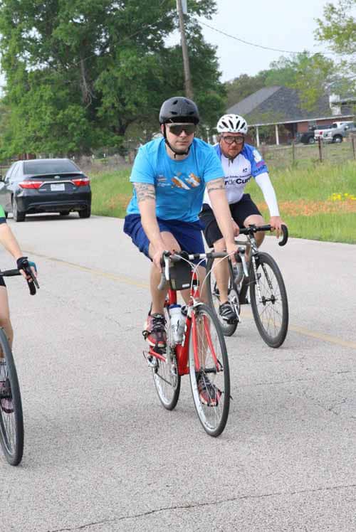 Bright blue bike jersey, pedaling on a scenic road during Bluebonnet Express cycling event.