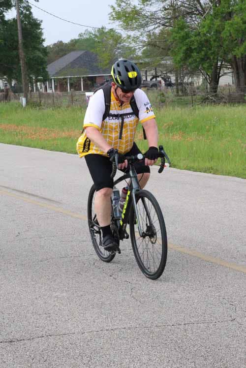 Cyclist riding on the road during daytime with greenery and houses in the background.