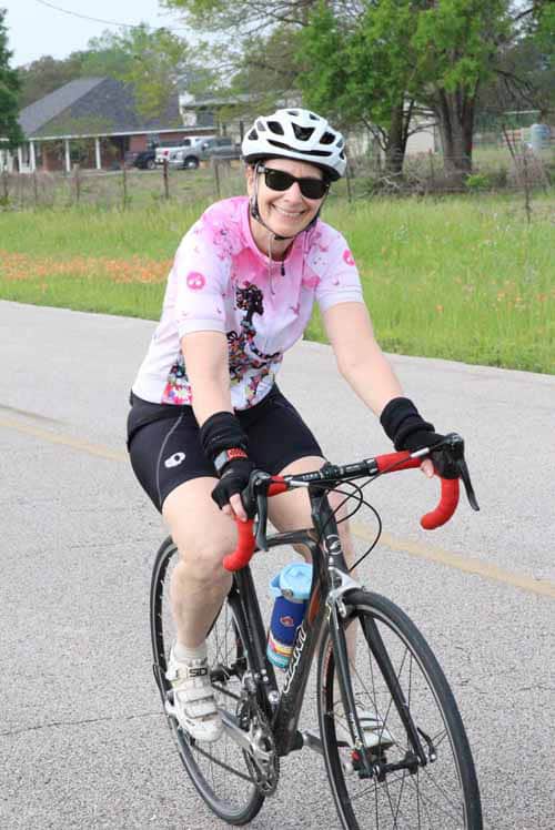Woman cycling outdoors in pink jersey and helmet, enjoying a ride on a sunny day.