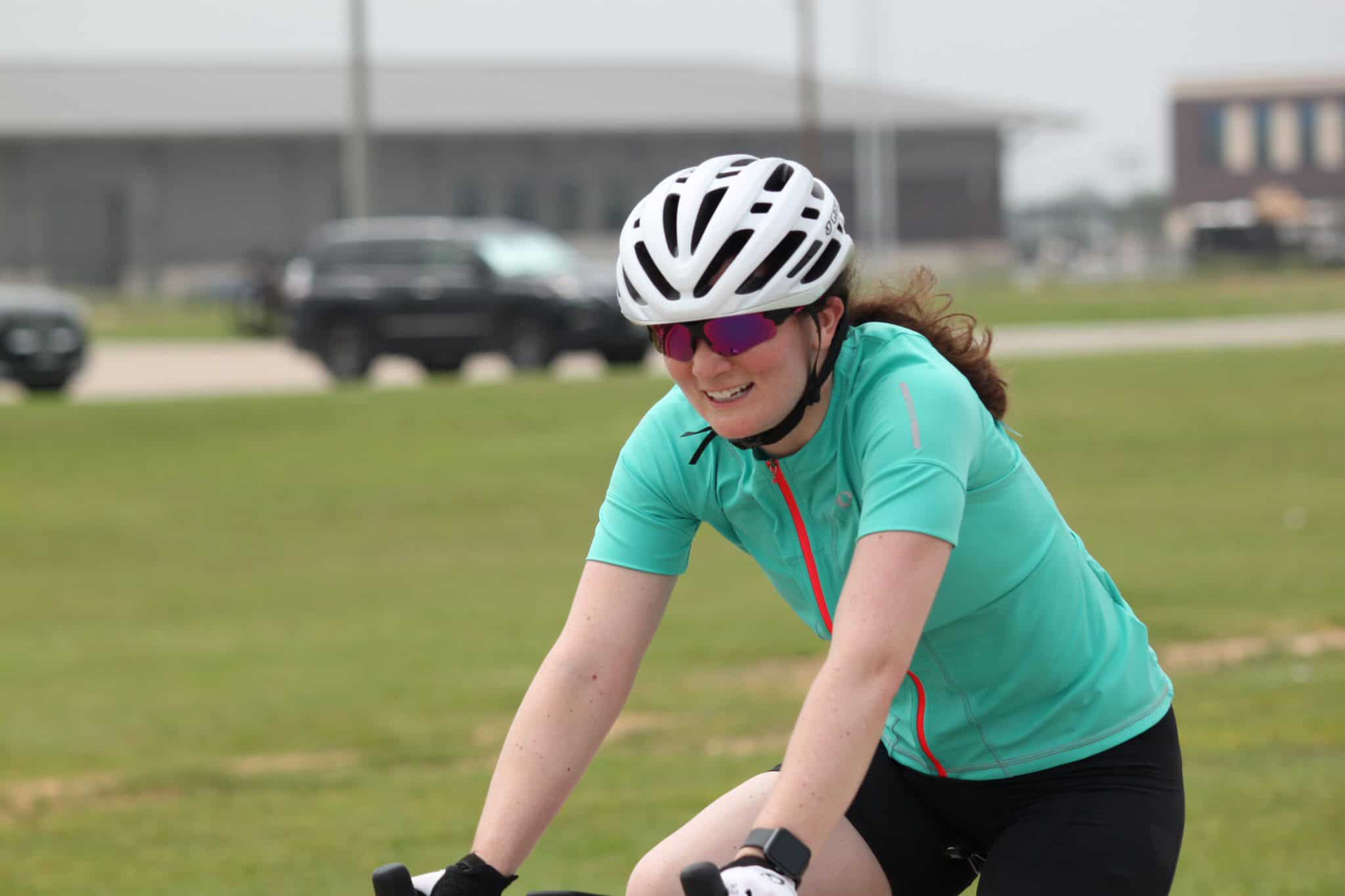 Vibrant woman cycling outdoors on a bright day, wearing a blue sports jersey, helmet, and sunglasses.