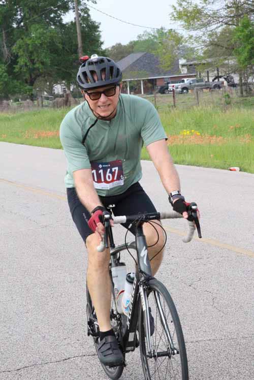 Active cyclist wearing helmet and race number during Bluebonnet Express ride on a rural road.