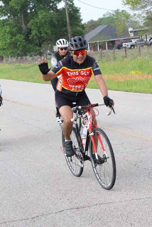Bright male cyclist wearing a colorful jersey, riding a red and white bike during Bluebonnet Express event.