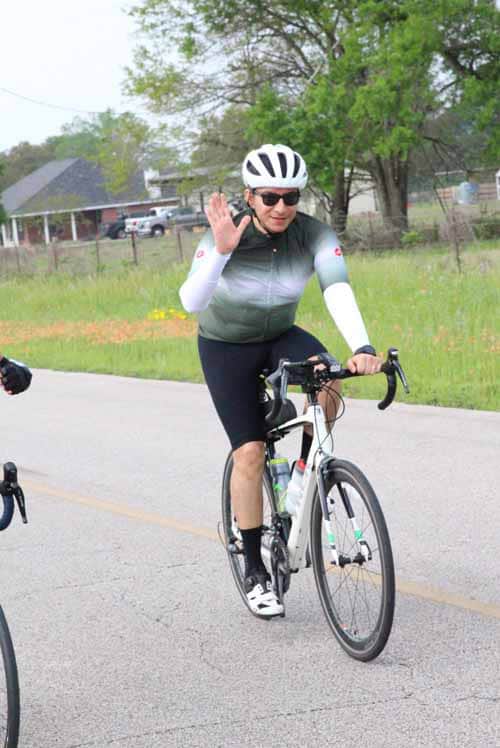 Cute cyclist wearing helmet and sunglasses waving on scenic outdoor ride.