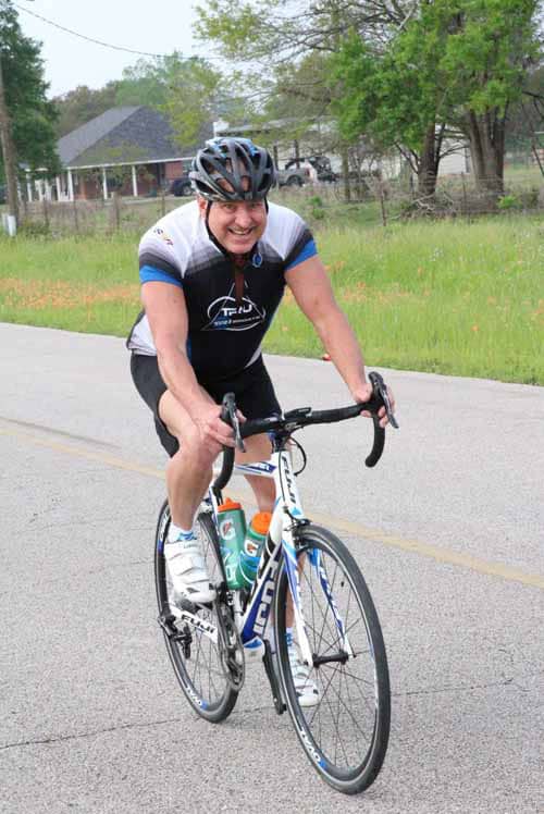 1. Smiling cyclist riding a road bike during Bluebonnet Express race.