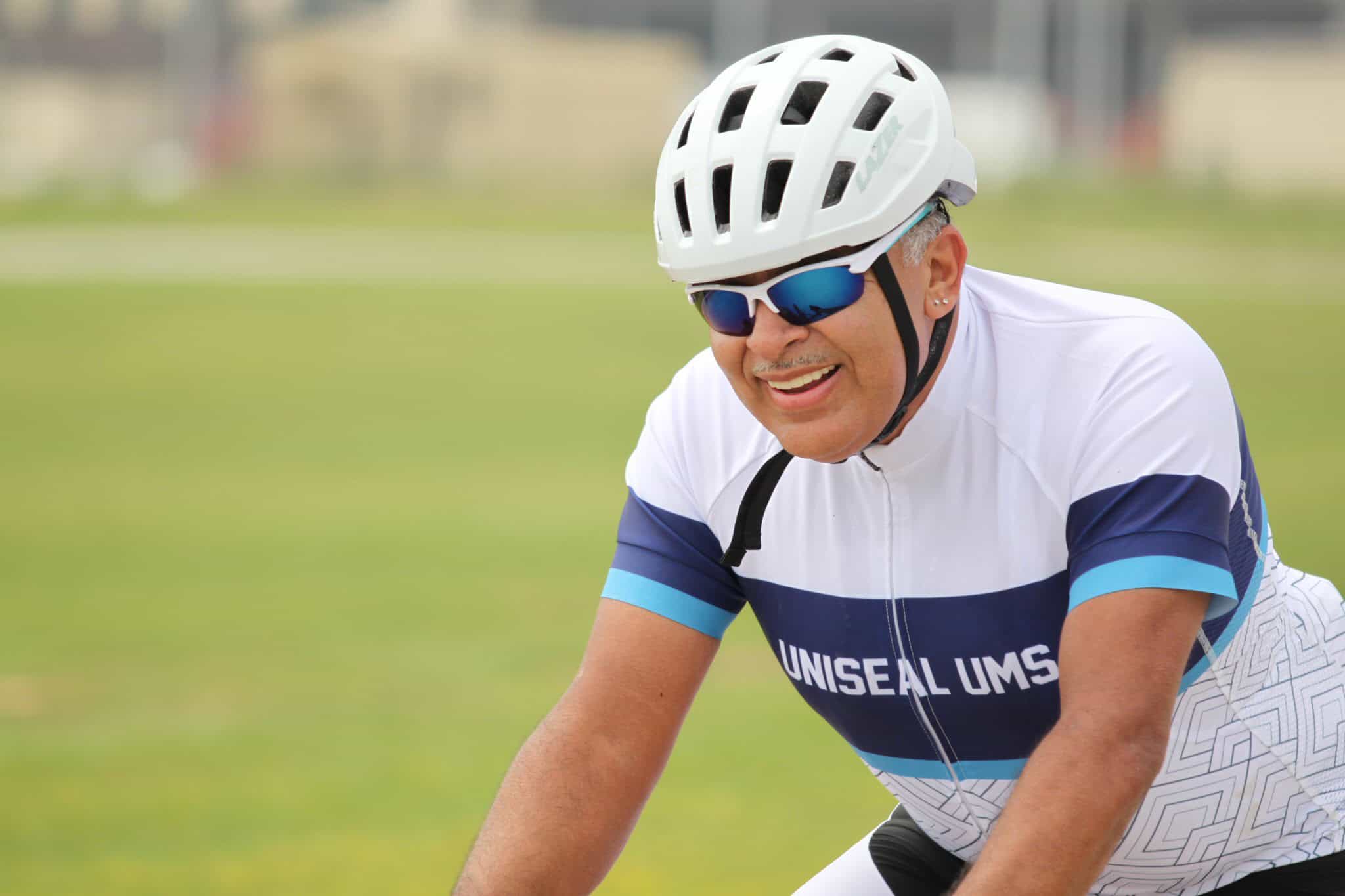 Active senior cyclist smiling on a bike, wearing helmet and sunglasses, enjoying outdoor riding.