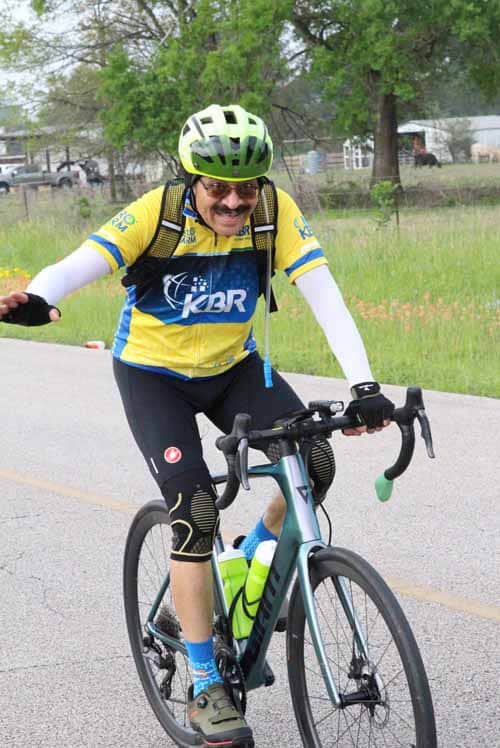Bright cyclist riding a blue road bike on a countryside road during daytime.