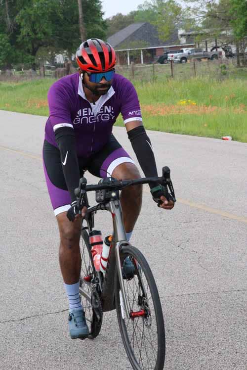 Bright purple cycling jersey and shorts with Red Blue helmet on a road bike outdoors.