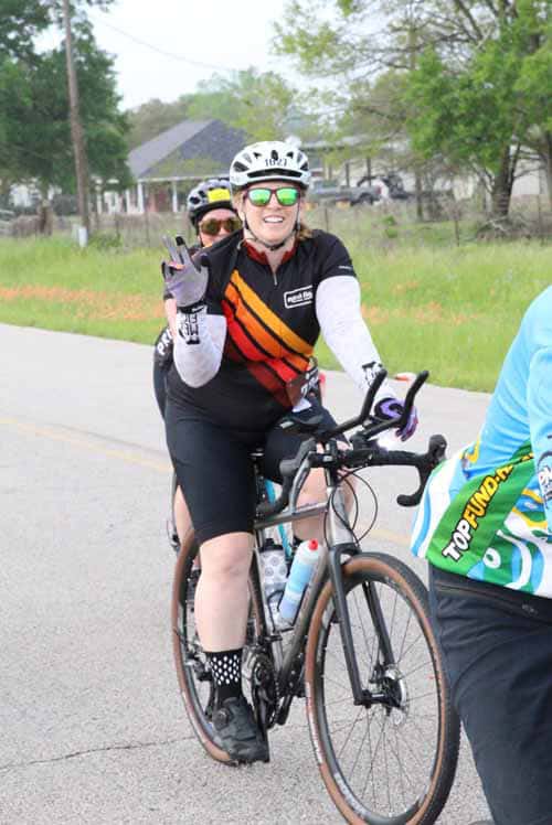 1. Female cyclist wearing helmet and sunglasses, smiling on her bike during Bluebonnet Express event.