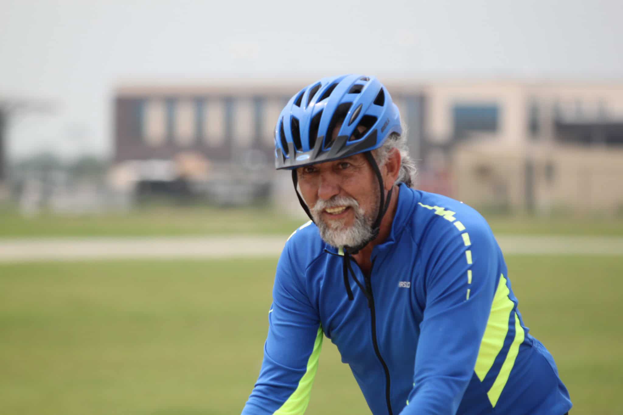 Bright elderly man riding a bike on a sunny day wearing a helmet and sports attire.