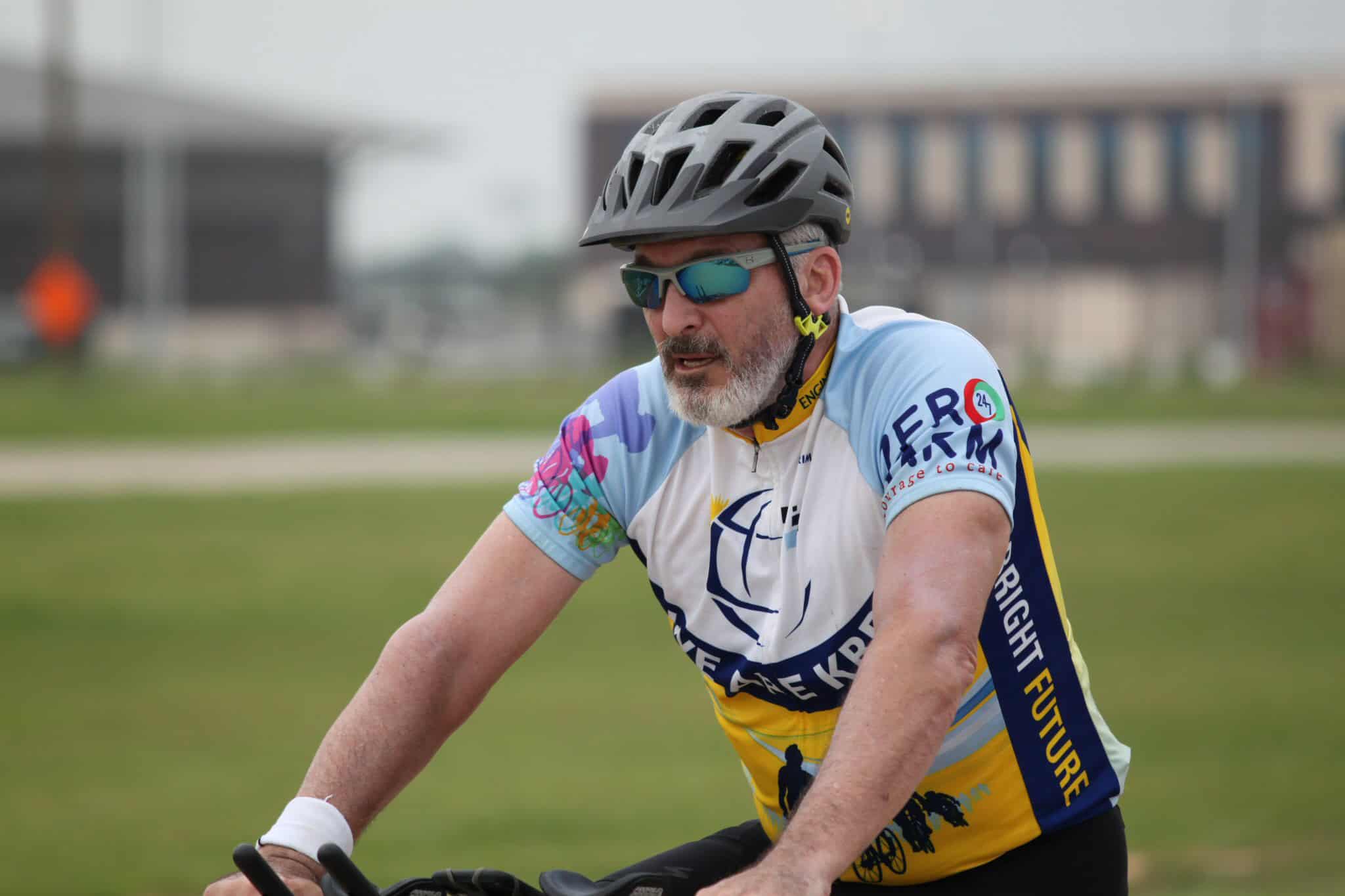 Senior cyclist wearing helmet and sunglasses riding bike outdoors during daytime.