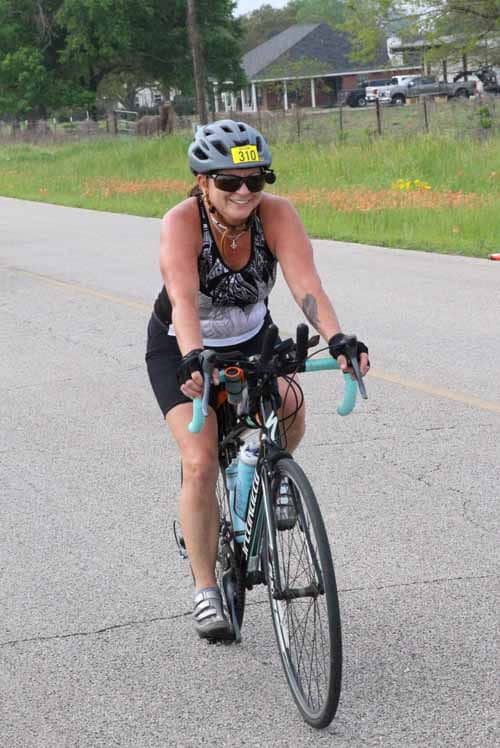 Bright female cyclist riding a road bike during Bluebonnet Express event, smiling and enjoying the ride.