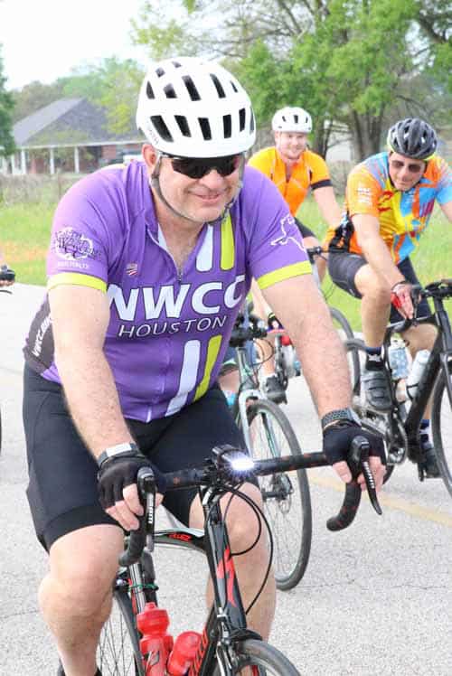 Bright-eyed cyclist wearing purple NWCC Houston jersey, participating in Bluebonnet Express bike ride.