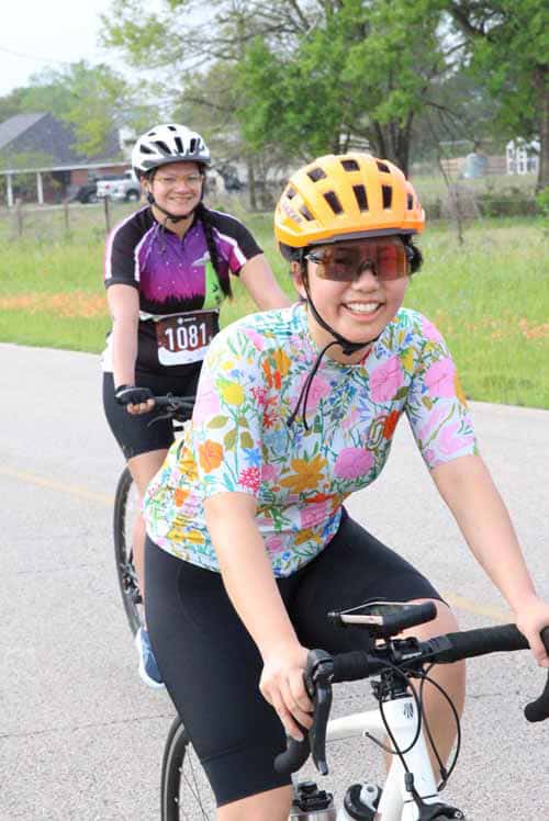 Smiling women riding bicycles outdoors, wearing helmets, enjoying sunny day, promoting healthy cycling lifestyle.
