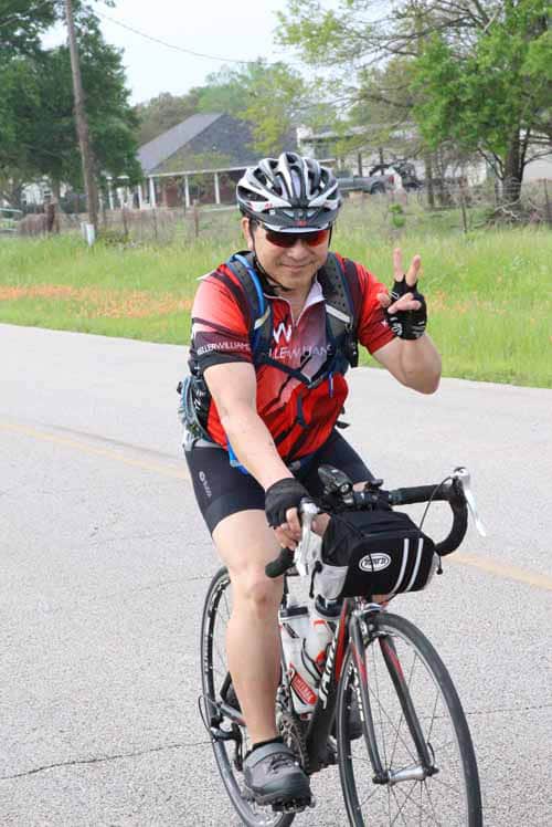 Stylish cyclist smiling on a bike ride during daytime, wearing helmet and sunglasses.