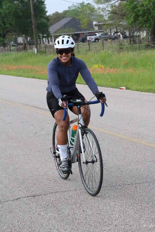 Bright woman cycling on a scenic road during daytime, wearing riding gear and helmet for outdoor exercise.