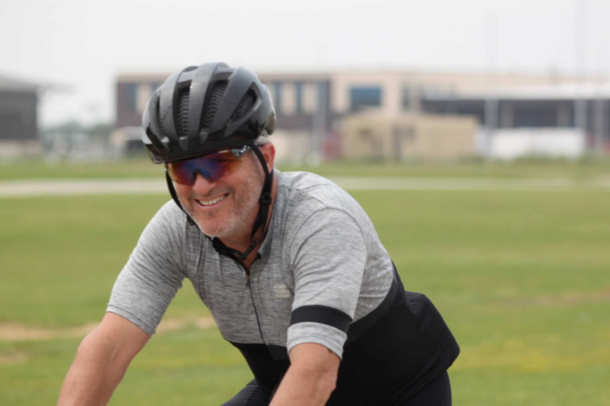 Man riding a bicycle with a helmet and sunglasses on green park bike trail.