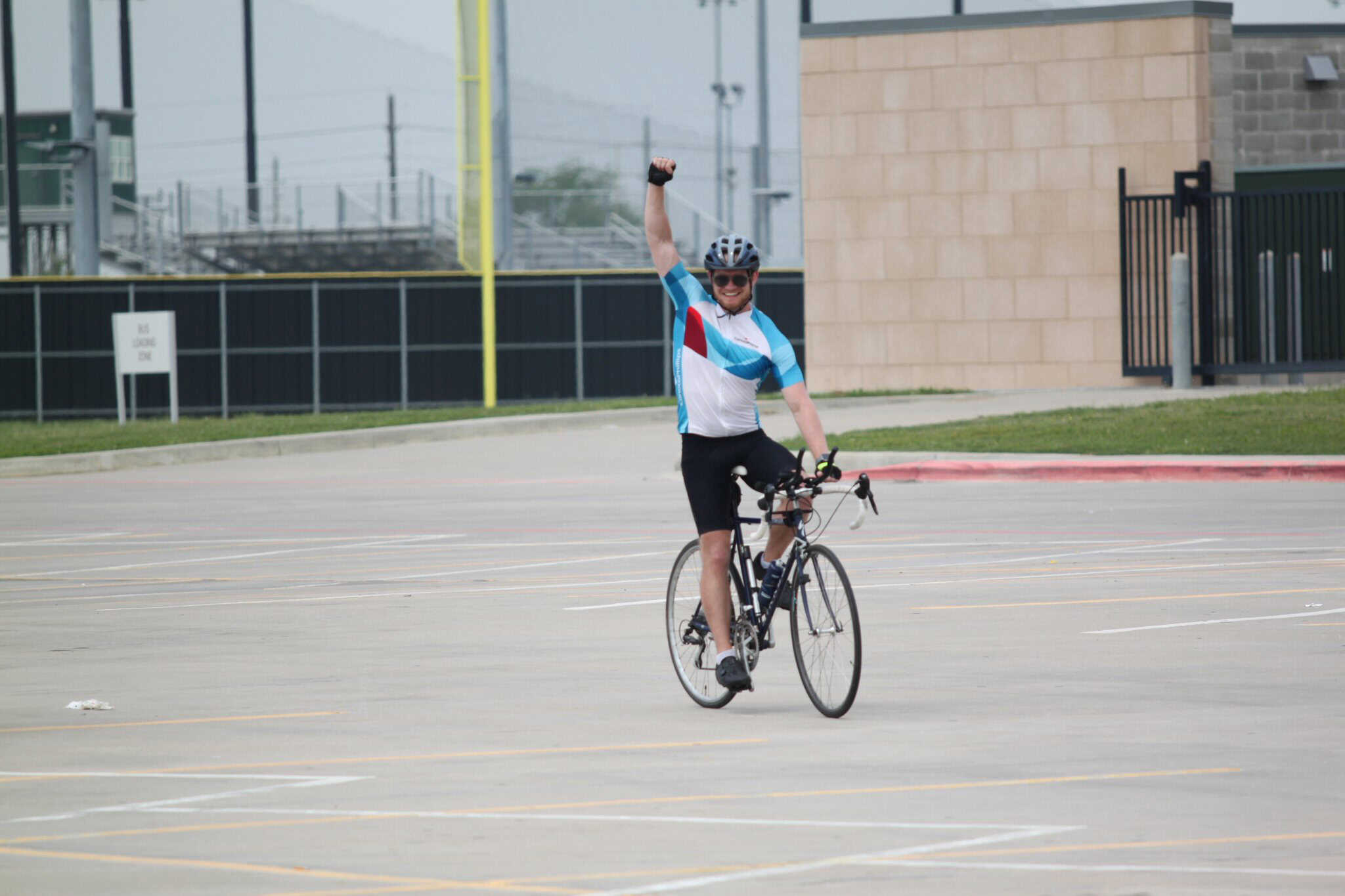 Bright male cyclist celebrating victory in an empty parking lot with Bluebonnet Express-themed cycling gear.