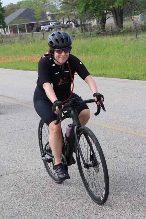 Comfortable woman riding a Black Road Bike on a scenic rural road during daytime.