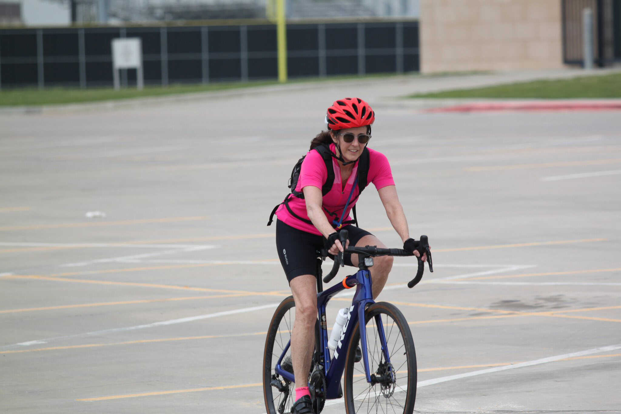 Bright woman cycling outdoors on Bluebonnet Express bike, wearing pink and red helmet.