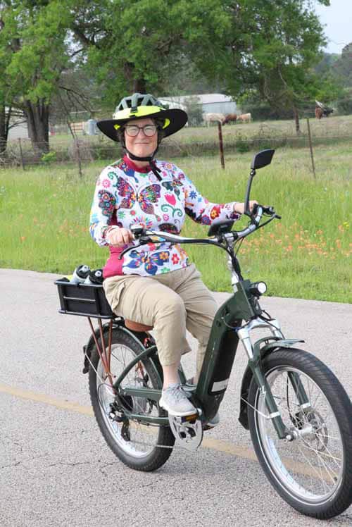 Bright woman riding electric bike on country road, enjoying outdoor cycling.