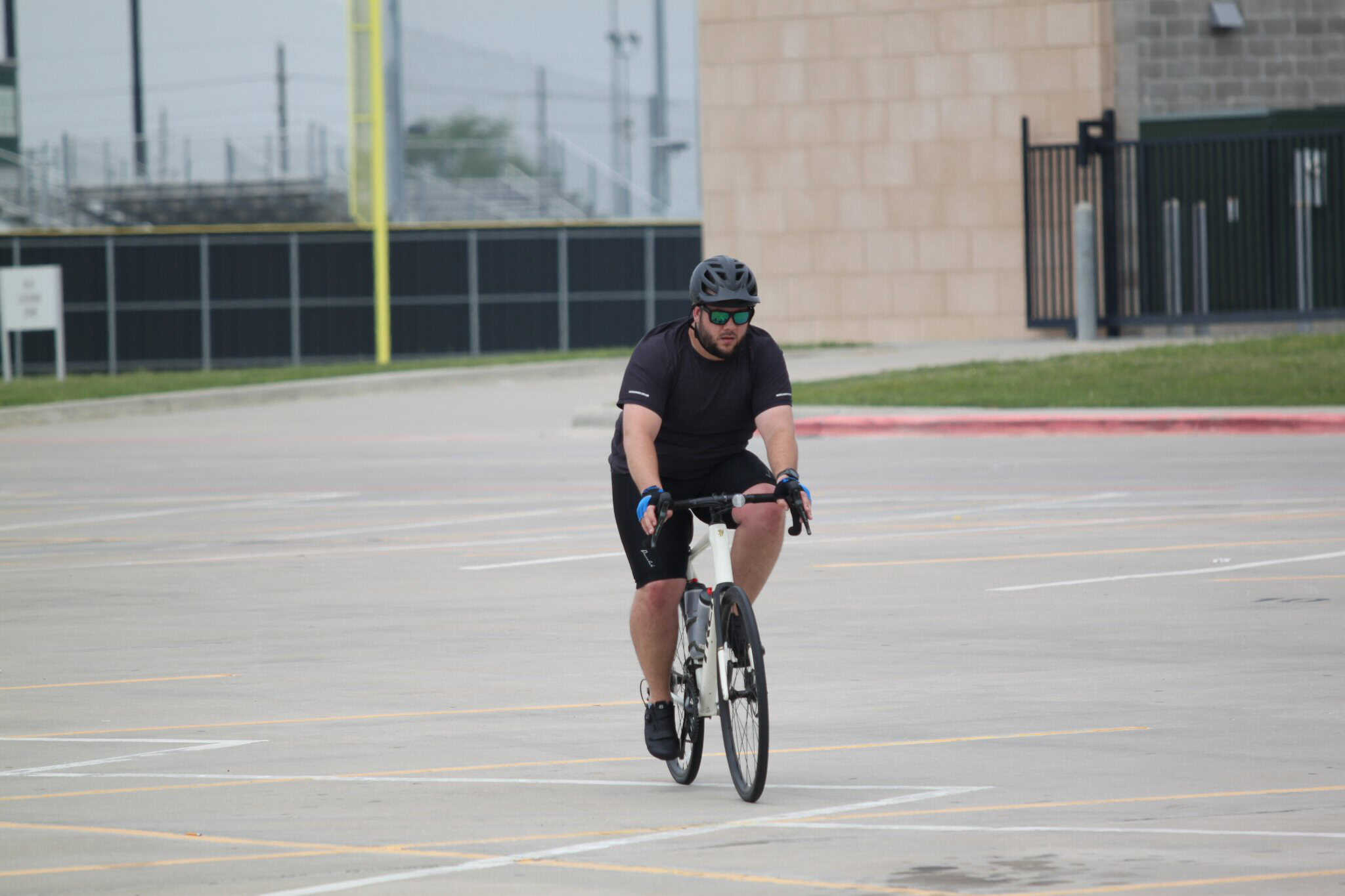 Man riding a bicycle in an empty parking lot, wearing a helmet and sunglasses, promoting eco-friendly transportation.