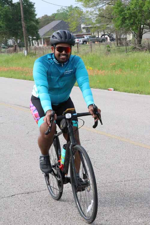 Vegan cyclist riding on rural road with Bluebonnet Express cycling gear, promoting eco-friendly bike tours.