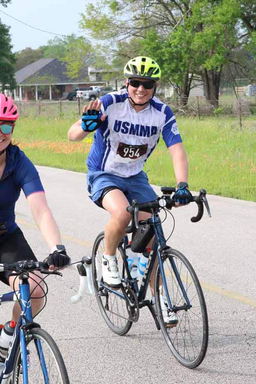 Bright smiling cyclist wearing USMMA jersey and helmet participating in Bluebonnet Express bike race.
