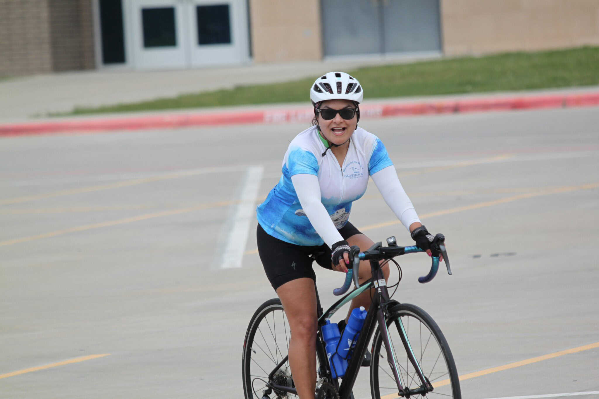 Bright female cyclist riding a bike during Bluebonnet Express event, wearing helmet and sunglasses.