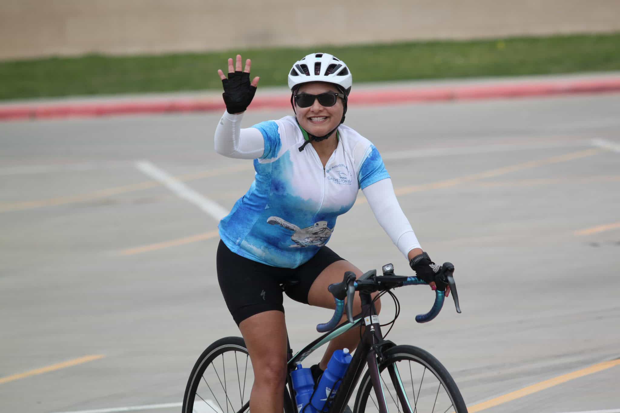 Joyful woman rides bike at Bluebonnet Express event, waving and smiling.