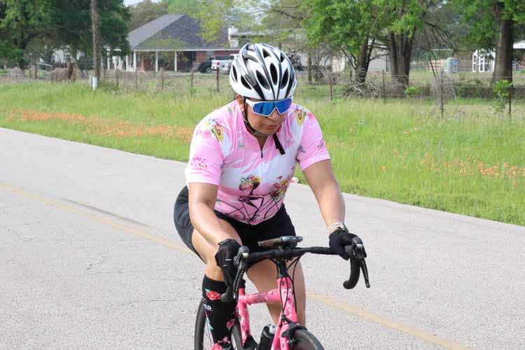 Bright female cyclist riding a pink bike on a scenic rural road during daytime.