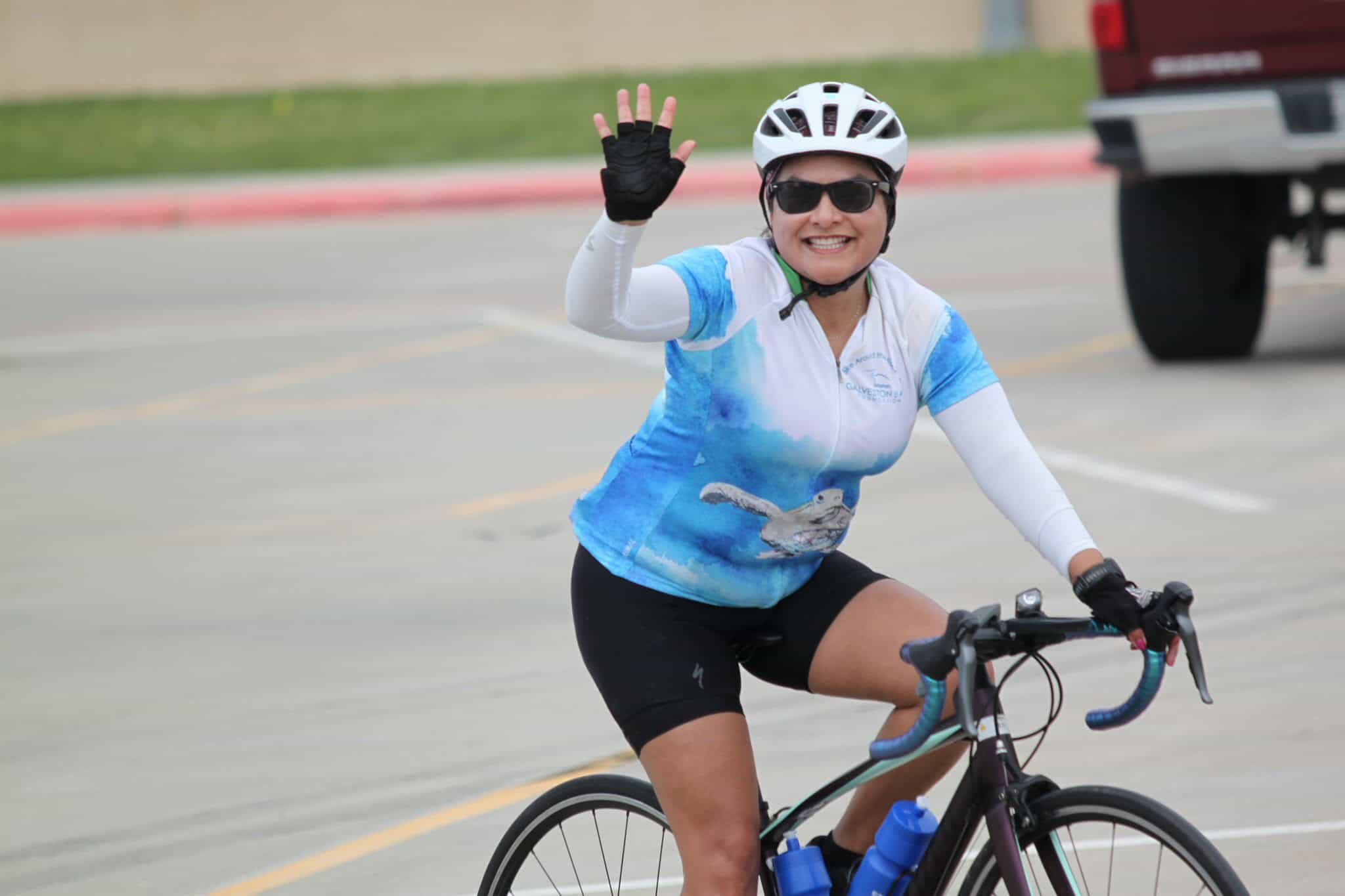 Vibrant cyclist waving while riding bluebonnet themed bike during a fun event.