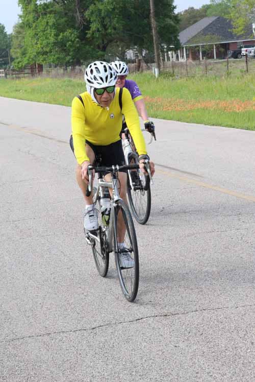 Cyclists riding on a scenic rural road during daytime, promoting outdoor biking and healthy lifestyle.