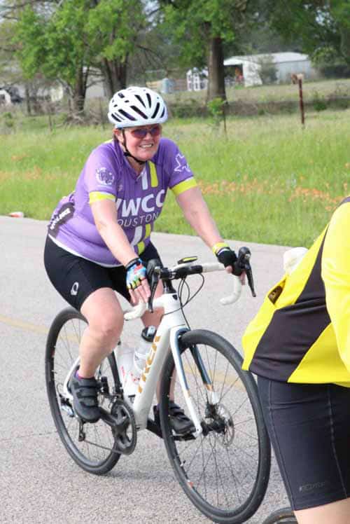 Bright woman cycling in purple jersey during Bluebonnet Express event, cheerful and energetic.
