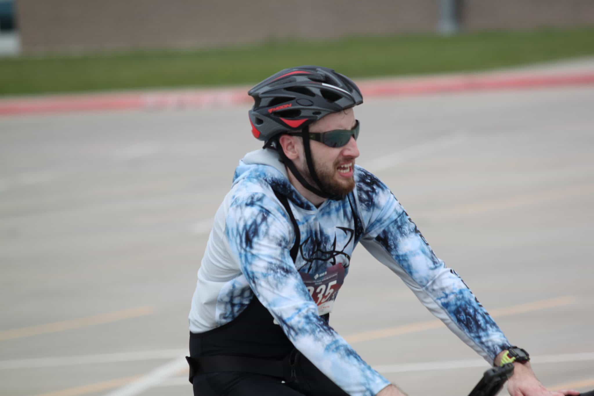 Enjoying a race on a custom cycling jersey with Bluebonnet Express branding, wearing a black helmet and sunglasses.