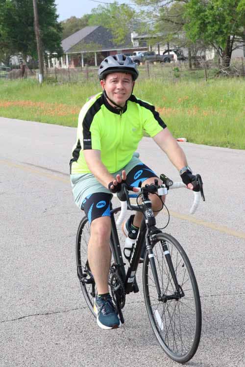 Bright cyclist in neon jersey riding a road bike on scenic rural route during daytime.