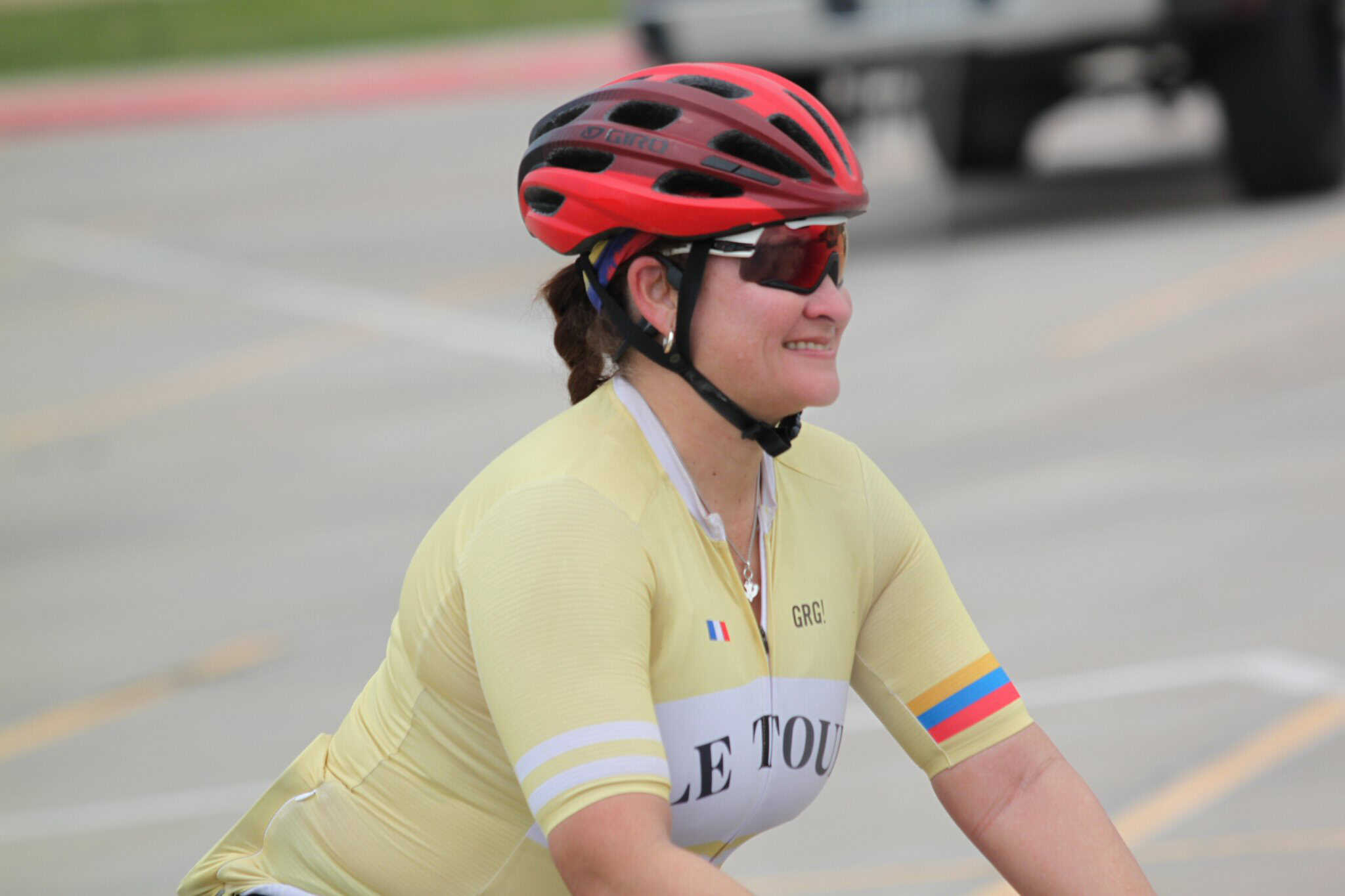 Woman cyclist wearing a red helmet and yellow jersey during Bluebonnet Express event, smiling and enjoying the ride.