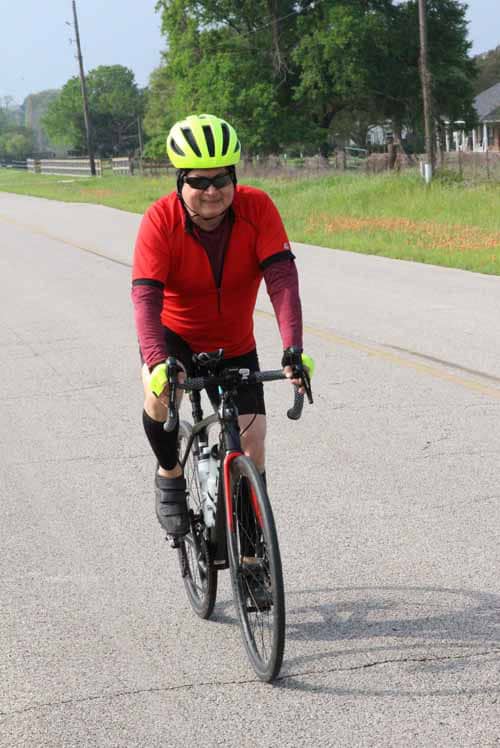 Bright cyclist riding a bike outdoors on a rural road with trees and houses in the background.