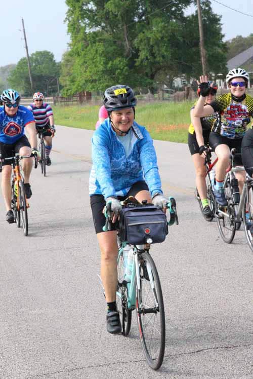 Joyful cyclist participating in Bluebonnet Express charity bike ride, smiling and waving.